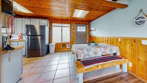 Ein gemütliches Blockhauszimmer mit Holzbalkendecke, einem Bett mit gemustertem Überwurf, einer Küchenzeile mit Edelstahlkühlschrank und einer Wanduhr.