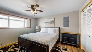 Ein Schlafzimmer mit Bett, Deckenventilator, Fenster, Nachttisch und Tür.