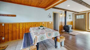 Ein Zimmer mit Holzwänden, einem Tisch mit gemustertem Tischläufer, einer Bank, einer kleinen Pflanze und einem Holzofen.