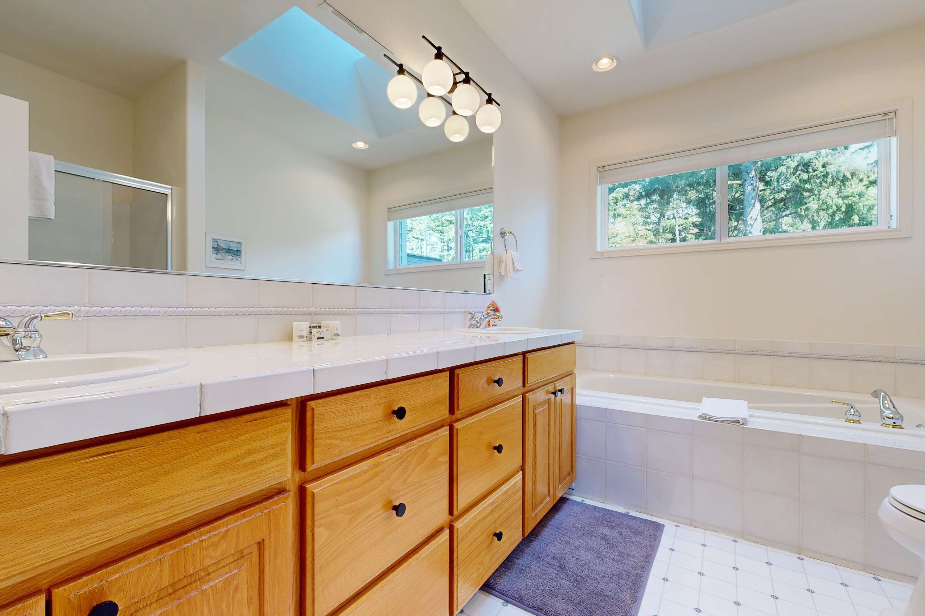 A modern bathroom with a large mirror, wooden vanity, dual sinks, and a bathtub.