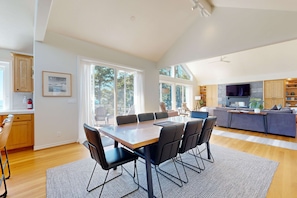 A modern kitchen with a dining area, large windows, and a built-in TV. - Idyllic Cape retreat with ocean views and private hot tub walk to state beach (Pacific City)