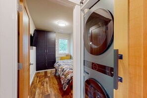 A compact room with a bed, a washing machine, and a built-in circular mirror. - Dog friendly brand new shipping container home steps from the beach (Pacific City)