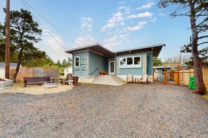 A two-story house with a gravel driveway, a front porch with a bench, and a wooden fence. - Dog friendly brand new shipping container home steps from the beach (Pacific City)