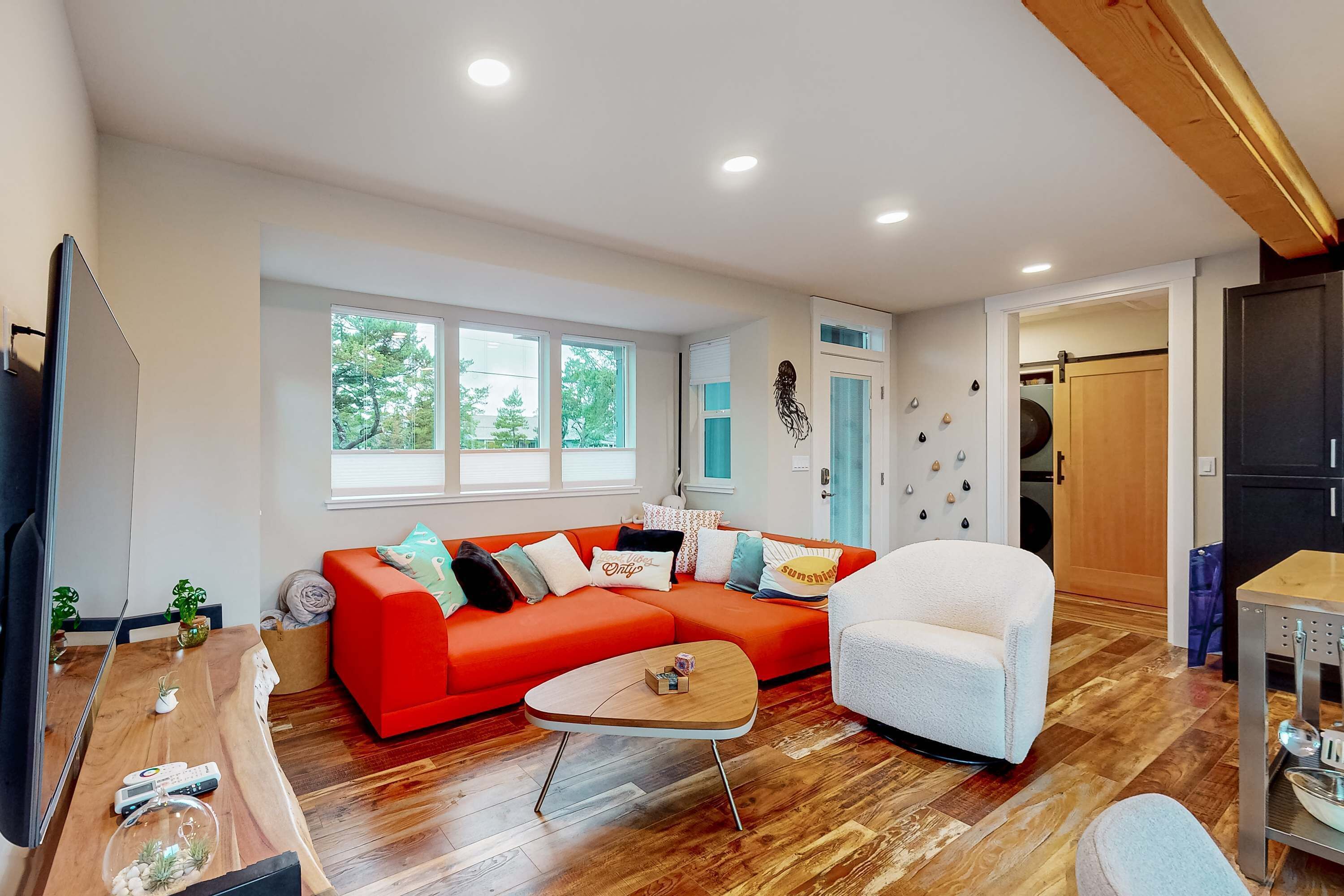 A modern living room with a red sofa, white armchair, wooden coffee table, and a dining area with a wooden table and chairs.