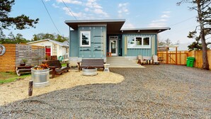 Una casa moderna de un piso con camino de entrada de grava, terraza de madera y una pequeña zona de estar al aire libre con mesa y sillas.