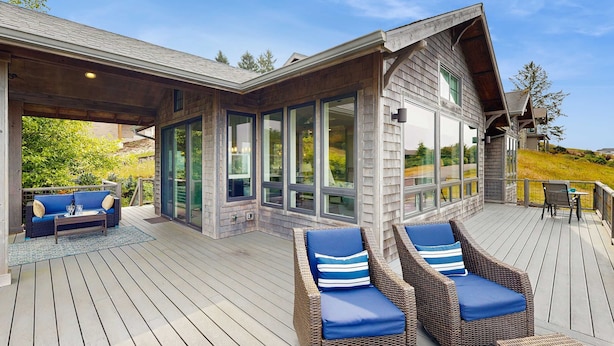 Une terrasse extérieure couverte, aménagée avec des meubles en osier et dotée de portes vitrées donnant accès à la maison.