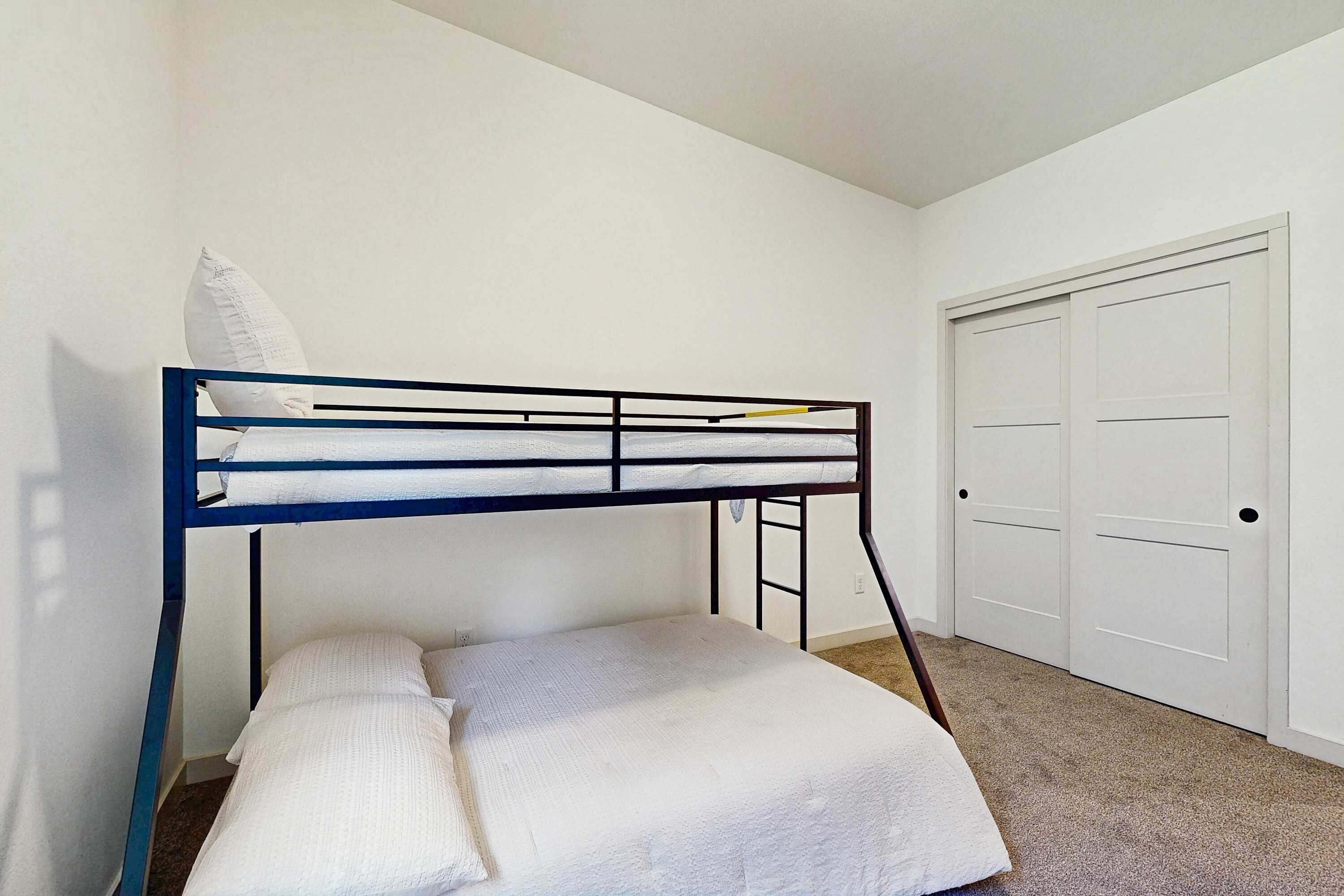A bunk bed with white bedding, a white door, and a carpeted floor.
