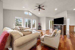 A spacious living room with a large TV, comfortable seating, and a ceiling fan. - Three story ocean view home with balconies grill and open layout dog friendly (Pacific City)