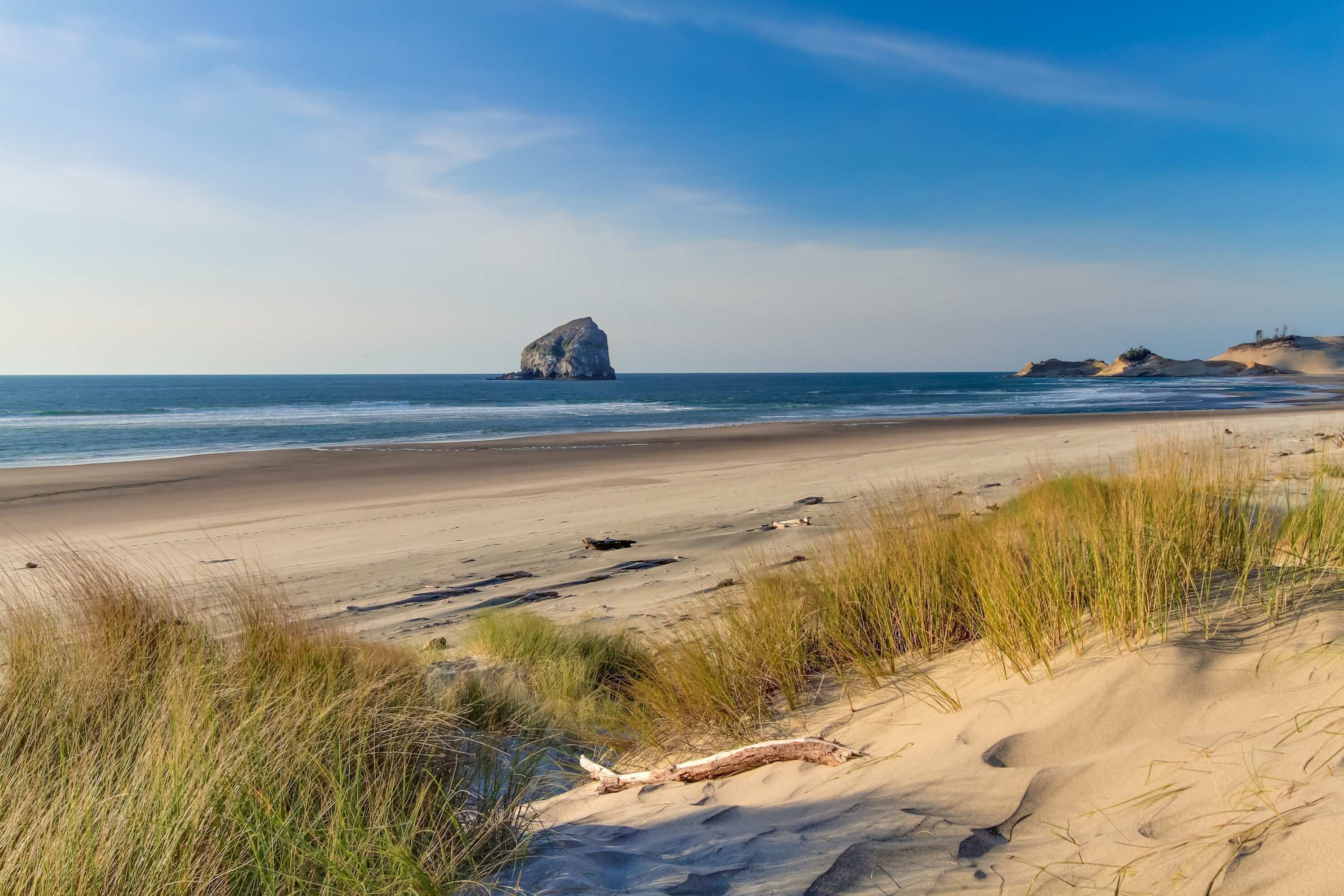 A beach with sand dunes, a rock formation, and the ocean.