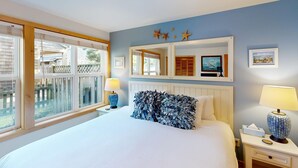 Un dormitorio con una cama grande, una mesita de noche con lámpara, una ventana con vista a una terraza, y una pared decorada con adornos de estrellas de mar.