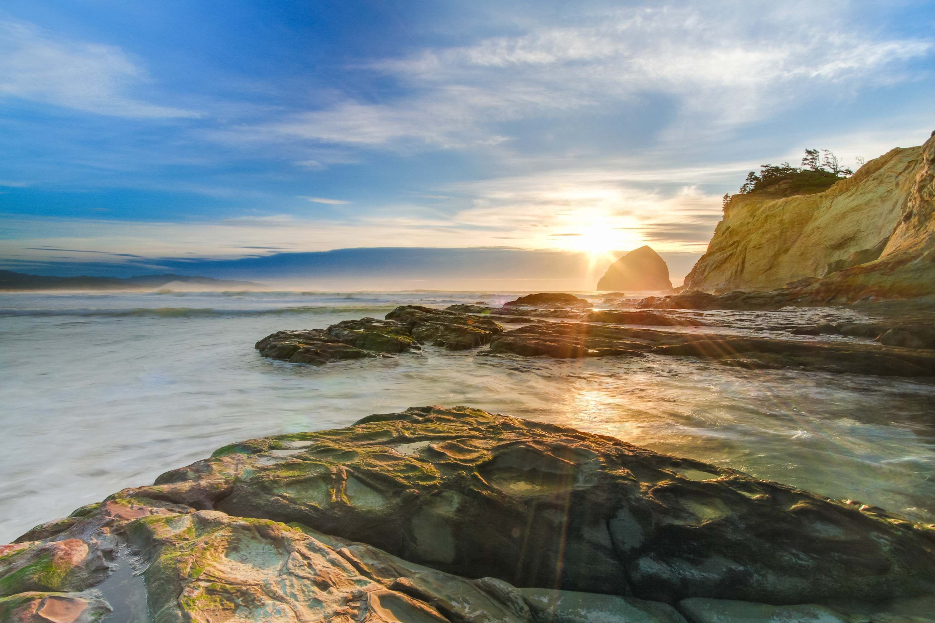 A coastal scene with a sunset, rocky shoreline, and a cliff.