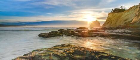 A coastal scene with a sunset, rocky shoreline, and a cliff.
