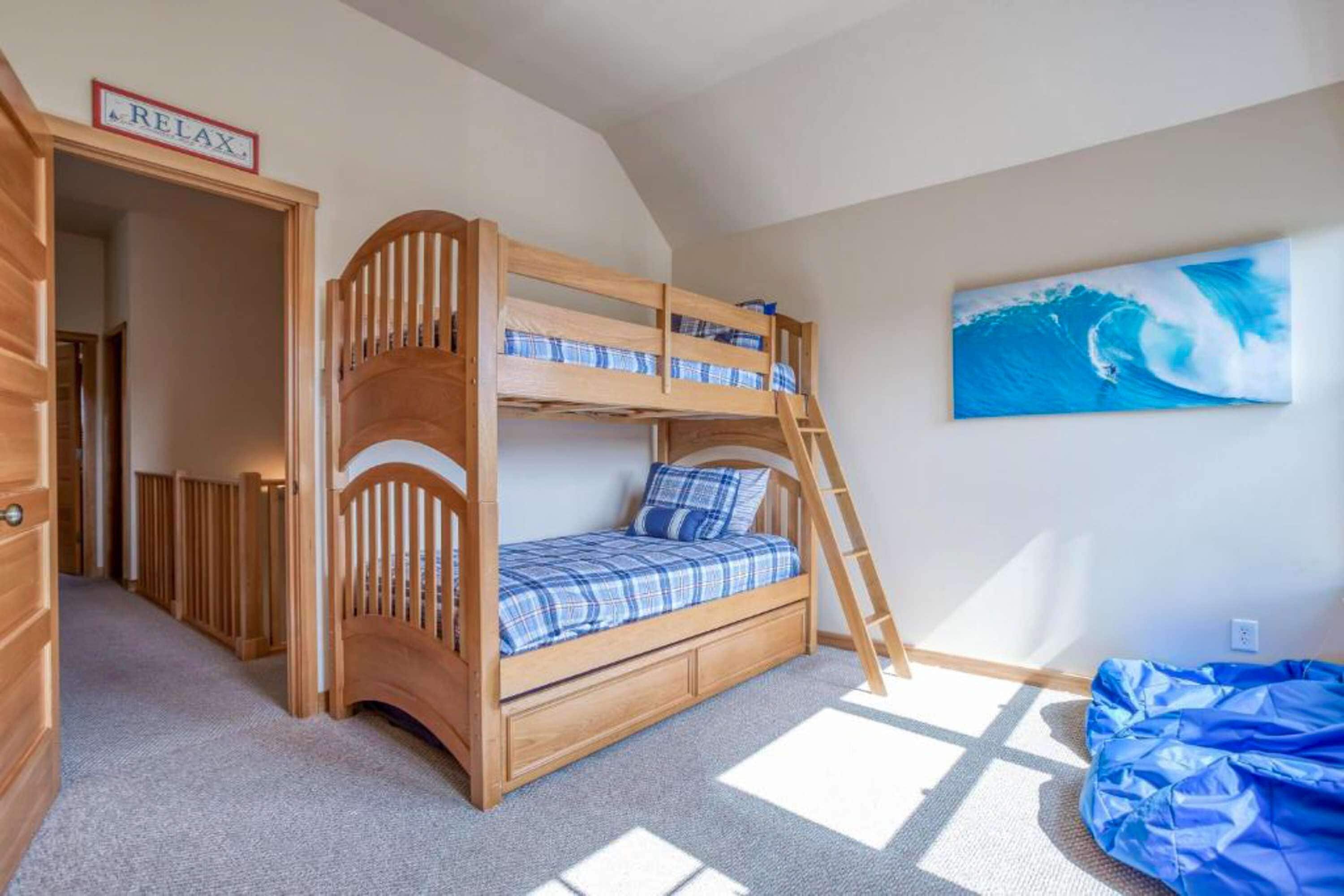 A bunk bed room with a 'RELAX' sign, a ladder, and a painting of a wave on the wall.