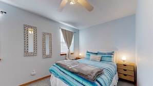 Ein Schlafzimmer mit Bett, Nachttischen, Deckenventilator und Zier-Spiegeln.