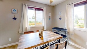 Ein Essbereich mit Holztisch, Stühlen, Deckenventilator und fensterbepflanzten Fenstern.