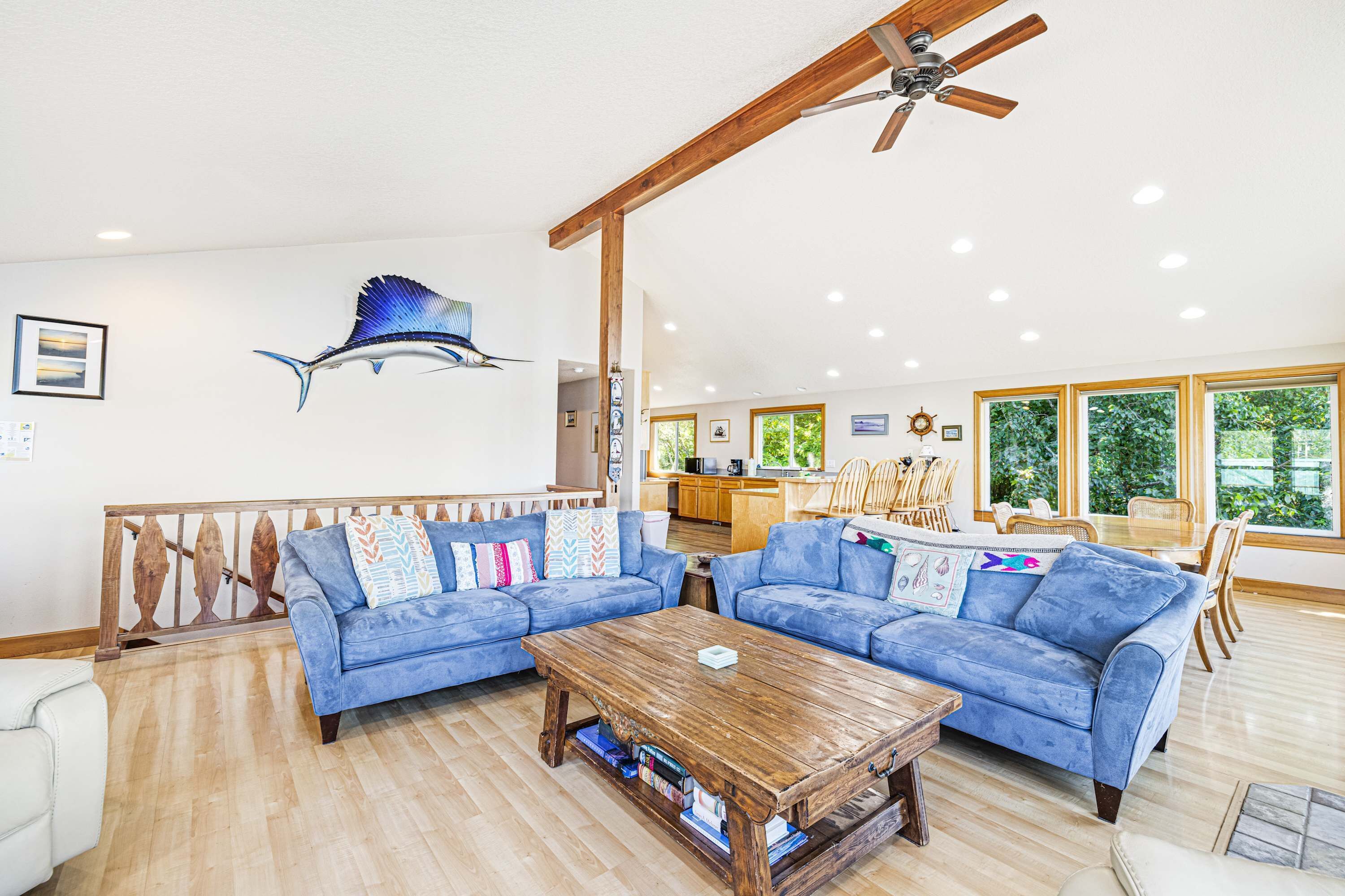 A spacious living room with a blue sofa set, a wooden coffee table, and a ceiling fan.