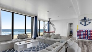 Un salon moderne doté d’une grande fenêtre donnant sur la plage, d’un fauteuil suspendu et d’un élément décoratif fixé au mur.