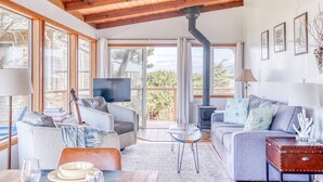 A spacious living room with a high ceiling, large windows, a fireplace, and a television. - Oceanfront cottage with hot tub beach access fireplace and WiFi Dog friendly (Cape Meares)