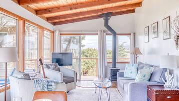 A spacious living room with a high ceiling, large windows, a fireplace, and a television.