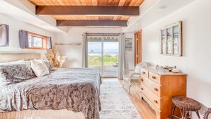 A bedroom with a bed, a dresser, a chair, and a view of the ocean. - Oceanfront cottage with hot tub beach access fireplace and WiFi Dog friendly (Cape Meares)