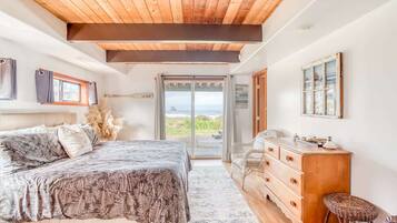 A bedroom with a bed, a dresser, a chair, and a view of the ocean.