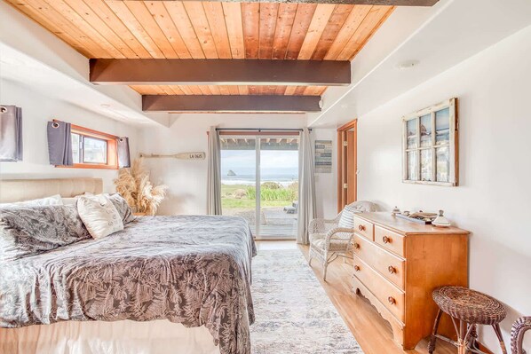 A bedroom with a bed, a dresser, a chair, and a view of the ocean. - Oceanfront cottage with hot tub beach access fireplace and WiFi Dog friendly (Cape Meares)
