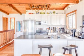 Una cocina con armarios blancos, electrodomésticos de acero inoxidable, techo de madera y una zona de bar con taburetes.