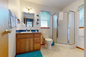 Een badkamer met een houten wastafelmeubel, toilet, douchecabine en een raam met zonwering.