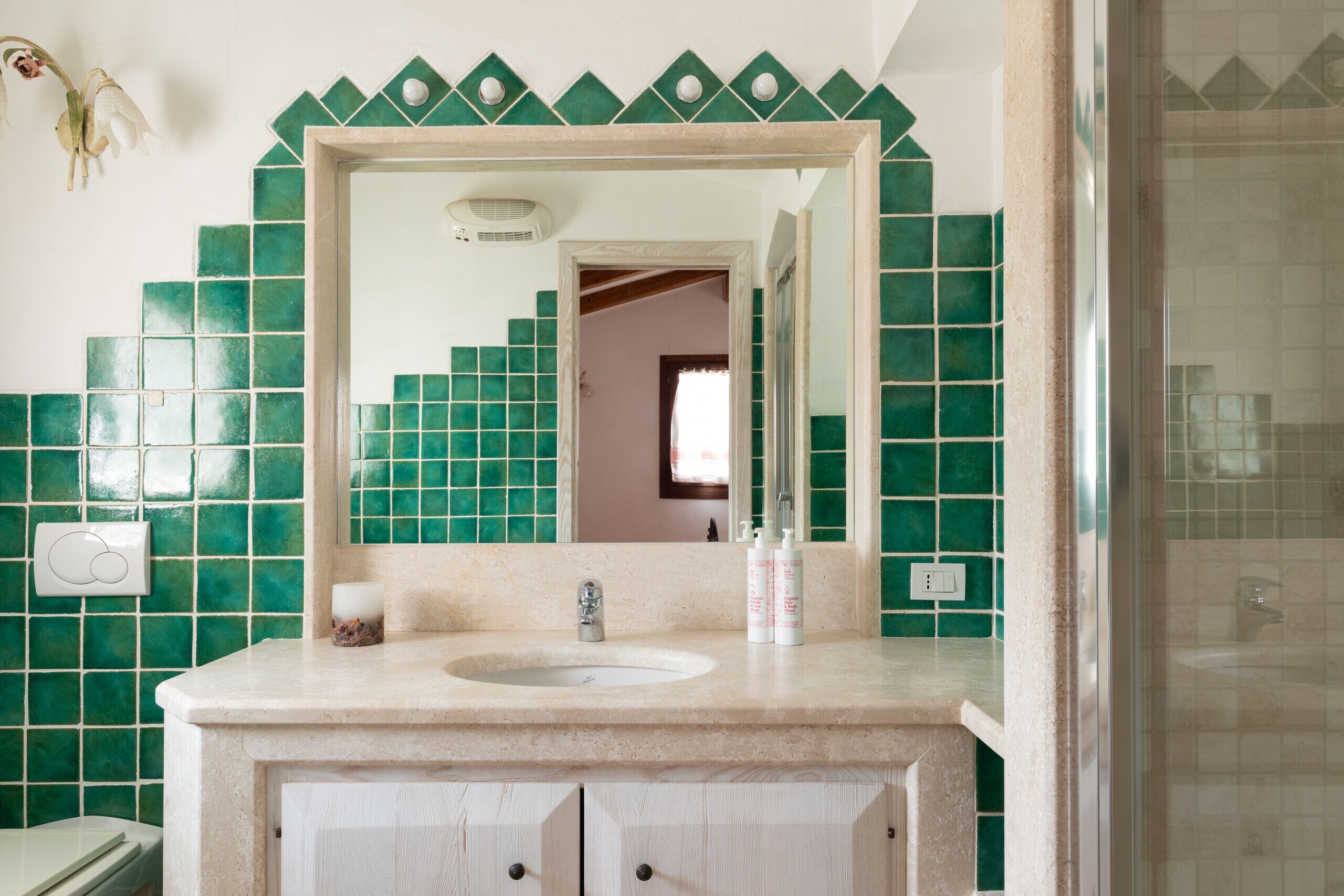 Un baño con lavamanos, espejo y paredes de azulejos verdes.