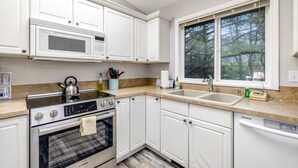 A kitchen with white cabinets, a microwave, stove, oven, sink, and a window with a view of trees. - Home with gas fireplace washer dryer and 2 outdoor spaces walk to beach (Tierra Del Mar)