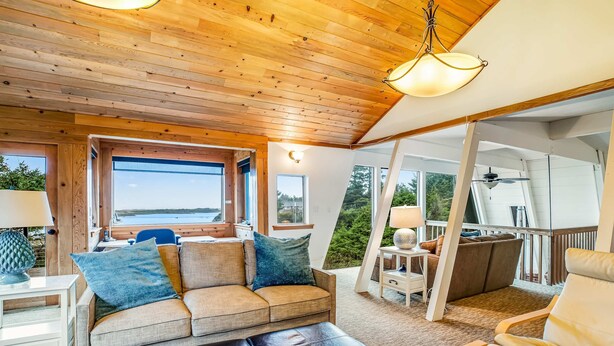 Cómoda sala de estar con techo de madera, sofá con cojines, mesa de centro y vistas al exterior.