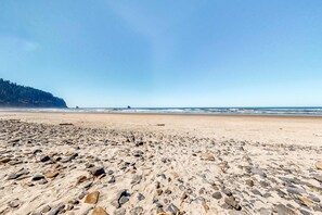Una playa con un primer plano rocoso y un acantilado boscoso al fondo.