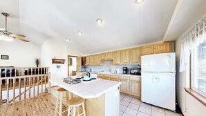 A kitchen with wooden cabinets, a white refrigerator, a bar stool, and a ceiling fan. - Family Friendly Coastal Home with Free WiFi Washer Dryer and Easy Beach Access (Cape Meares)