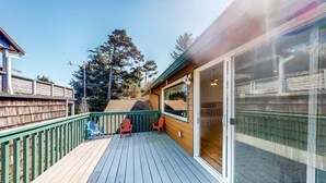 A wooden deck with two chairs, a glass door, and a view of trees. - Family Friendly Coastal Home with Free WiFi Washer Dryer and Easy Beach Access (Cape Meares)