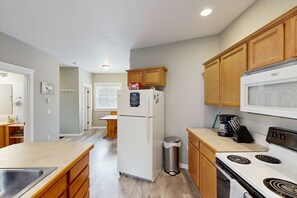 A kitchen with wooden cabinets, a white refrigerator, a stove, and a trash can. - Cozy Coast Escape, Close to the Beach, Family Friendly (Netarts)