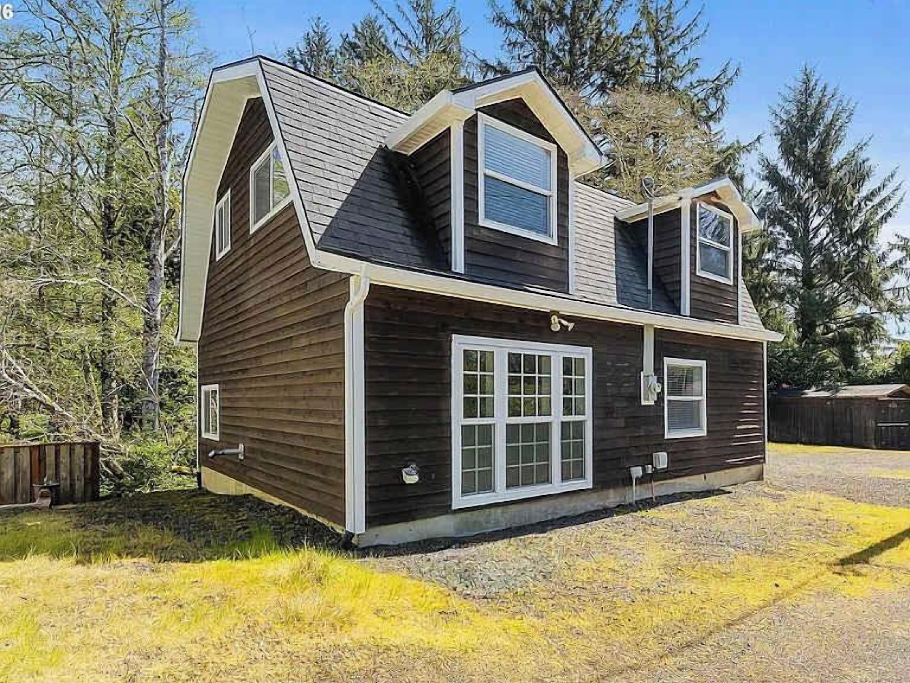 A two-story wooden house with a sloped roof, large windows, and a front porch.