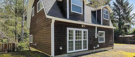 A two-story wooden house with a sloped roof, large windows, and a front porch.