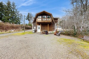 A wooden cabin with a balcony, gravel driveway, and a bench. - Cozy Coast Escape, Close to the Beach, Family Friendly (Netarts)