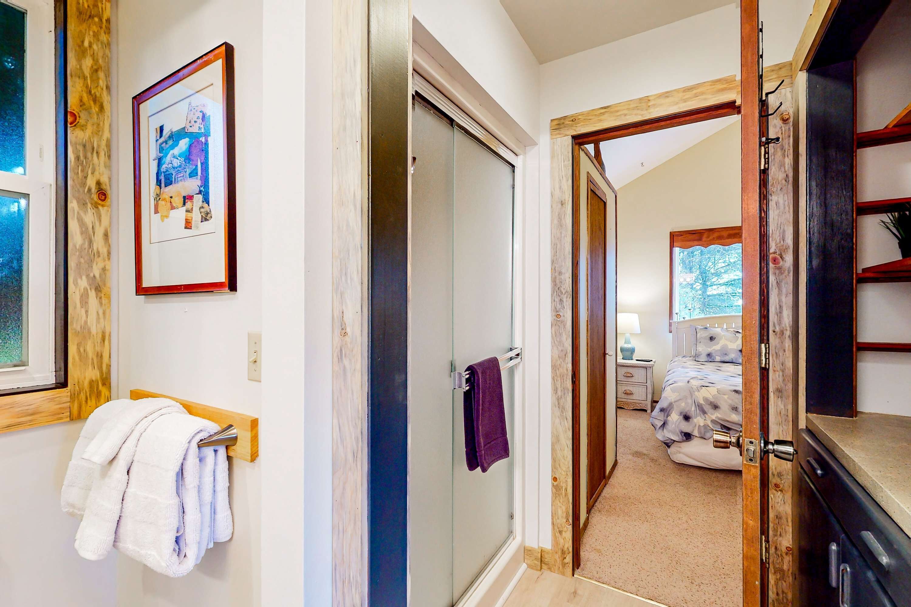 Une pièce dotée d’une porte vitrée donnant sur une salle de bain, d’un lit recouvert d’une couvre-lit à motifs floraux et d’une étagère en bois.