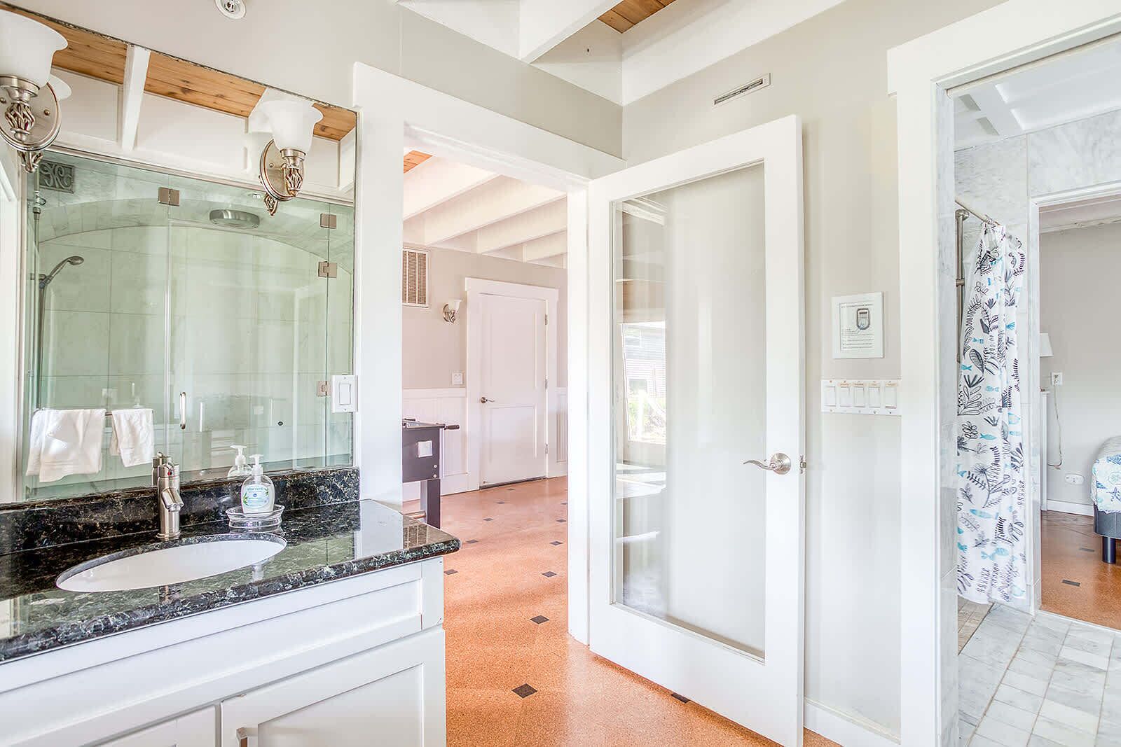 A modern bathroom with a glass shower, a marble sink, and a white door leading to another room.