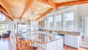 A spacious kitchen with a large island, wooden ceiling beams, and a view of the outdoors. - Elegant home with sauna private hot tub and ocean views accessible by elevator (Cape Meares)