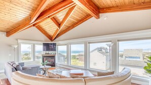 A spacious living room with a large white sofa, a fireplace, and large windows offering a view of the ocean. - Elegant home with sauna private hot tub and ocean views accessible by elevator (Cape Meares)
