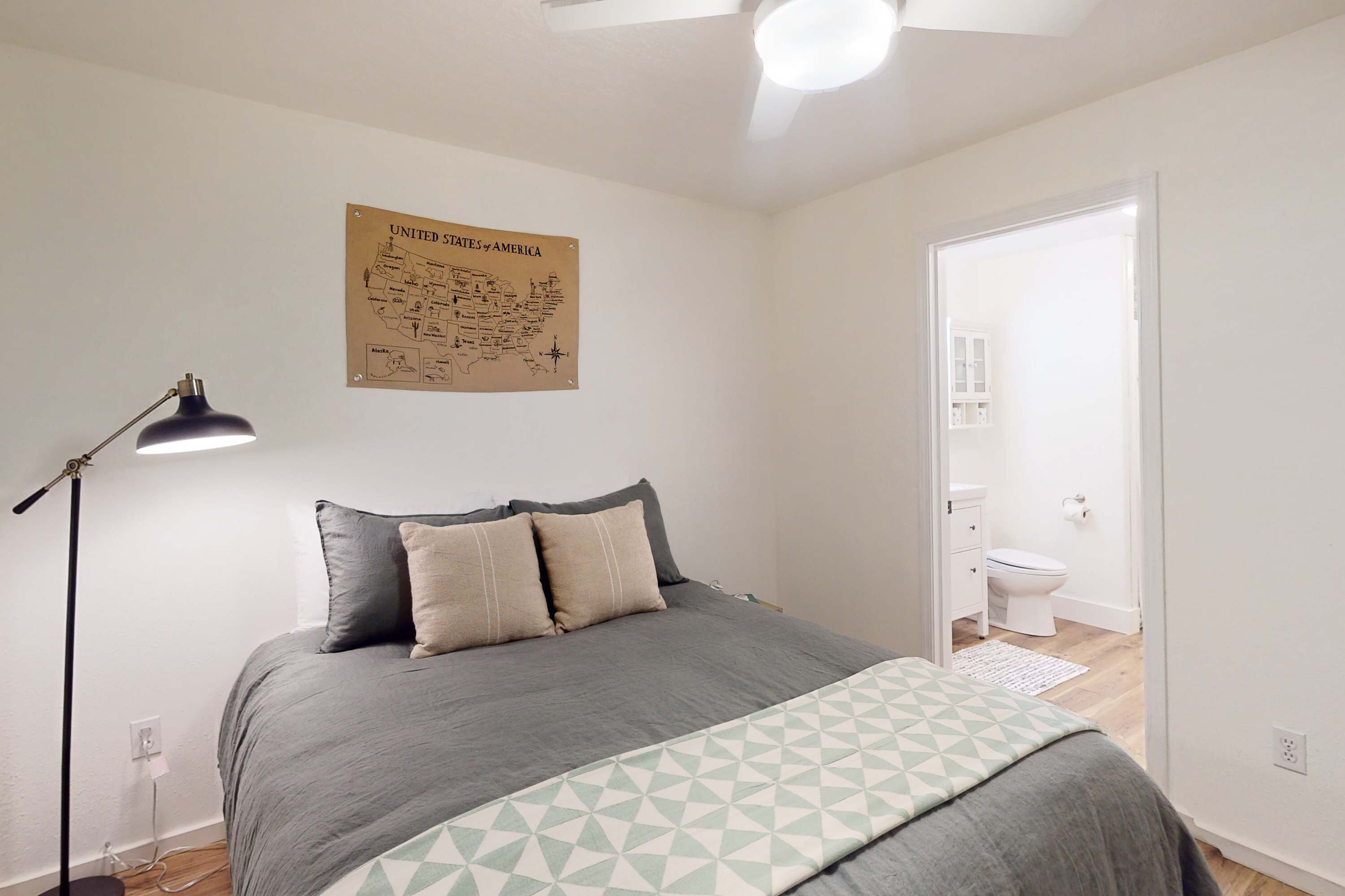 Una camera da letto con un letto, una lampada da terra, una mappa degli Stati Uniti appesa al muro e un bagno visibile attraverso una porta aperta.