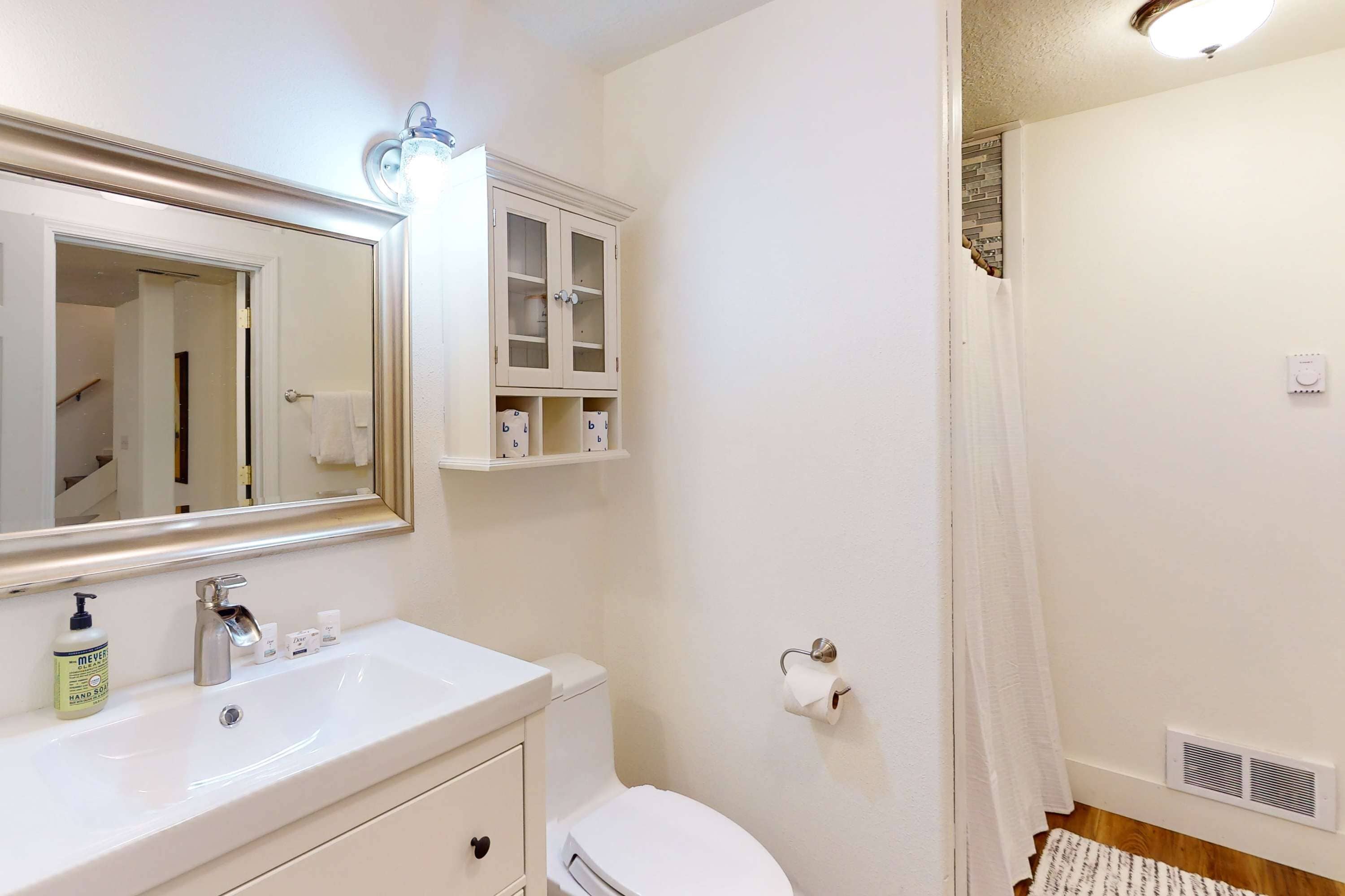 Ein Badezimmer mit weißem Waschbecken, Spiegel und Schrank, Toilette und Duschvorhang.