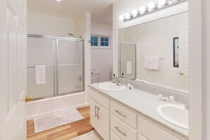 A modern bathroom with a glass-enclosed shower, two sinks, and a large mirror with lights. - Renovated three story home by the beach with a furnished deck and washer dryer (Cape Meares)