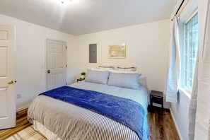 A bedroom with a bed, a nightstand, a door, and a window with curtains. - Renovated three story home by the beach with a furnished deck and washer dryer (Cape Meares)
