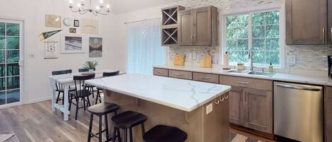 A modern kitchen with a large island, bar stools, and a dishwasher.