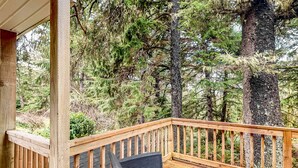 A wooden deck with a railing, surrounded by dense forest. - Renovated three story home by the beach with a furnished deck and washer dryer (Cape Meares)