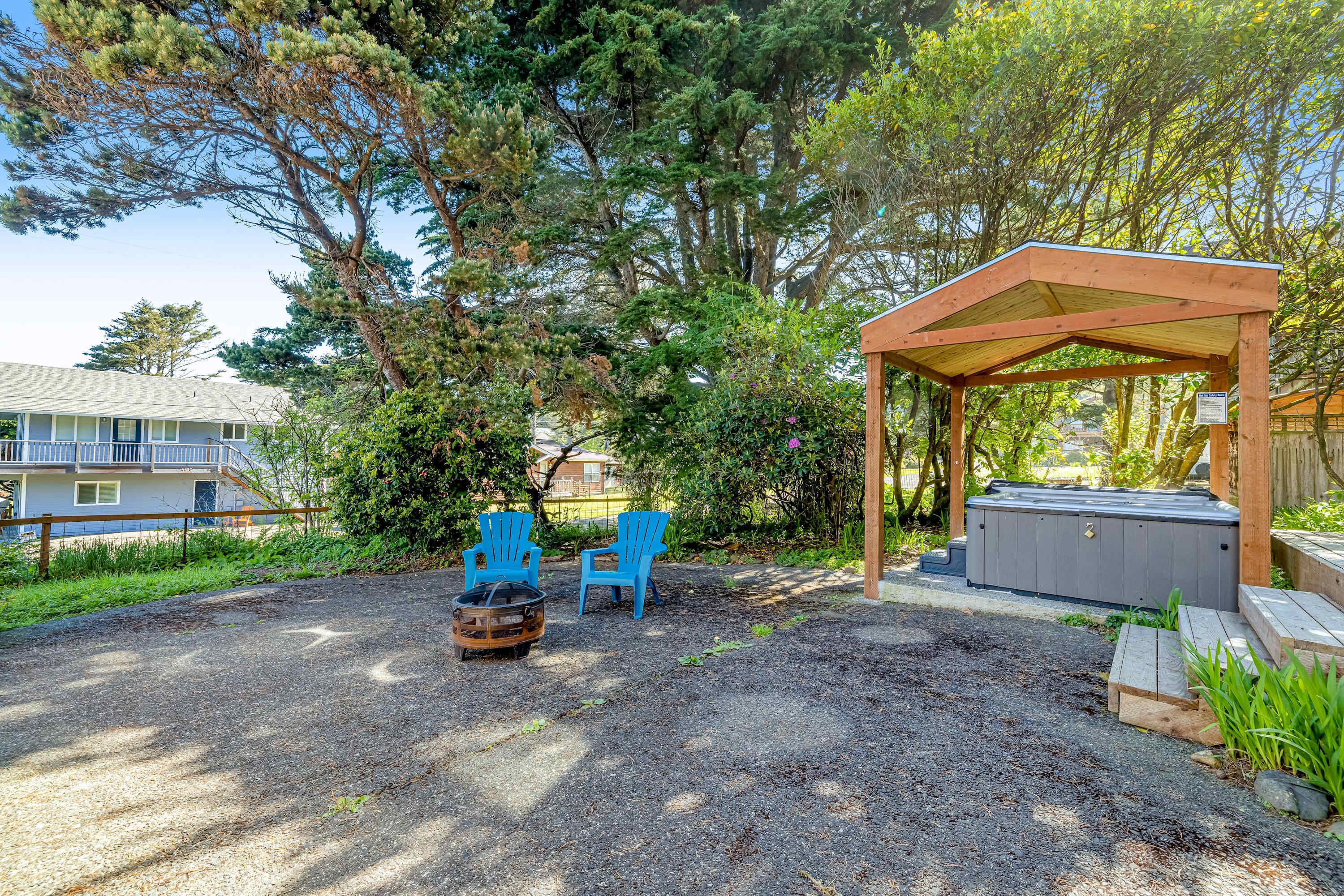A covered outdoor seating area with two blue chairs, a fire pit, and a hot tub.
