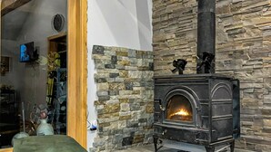 Una habitación acogedora con pared de piedra, chimenea y un otoman verde.